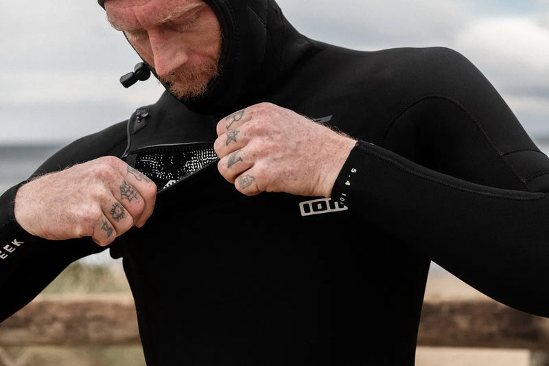 Person wearing a black wetsuit with visible branding, adjusting the hood outdoors. Front photo - urbaneight