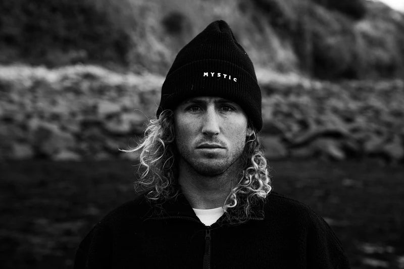 Person wearing a black beanie with 'Mystic' logo against a rocky background