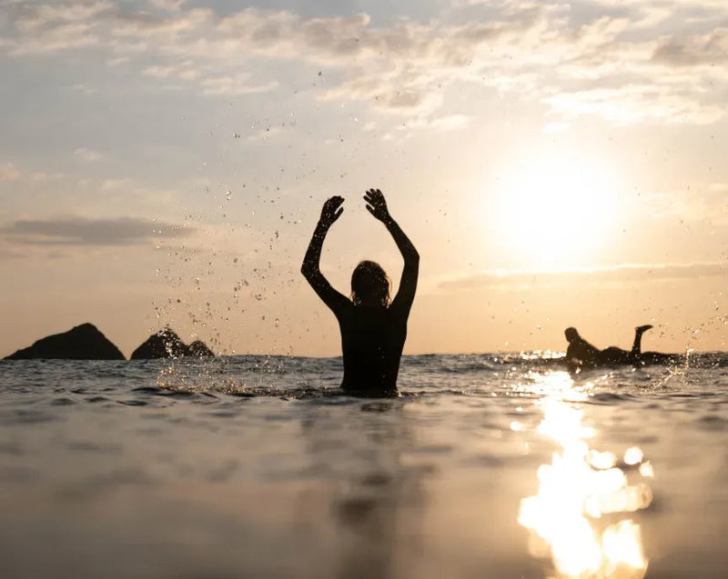 Person playing in the water with arms raised at sunset